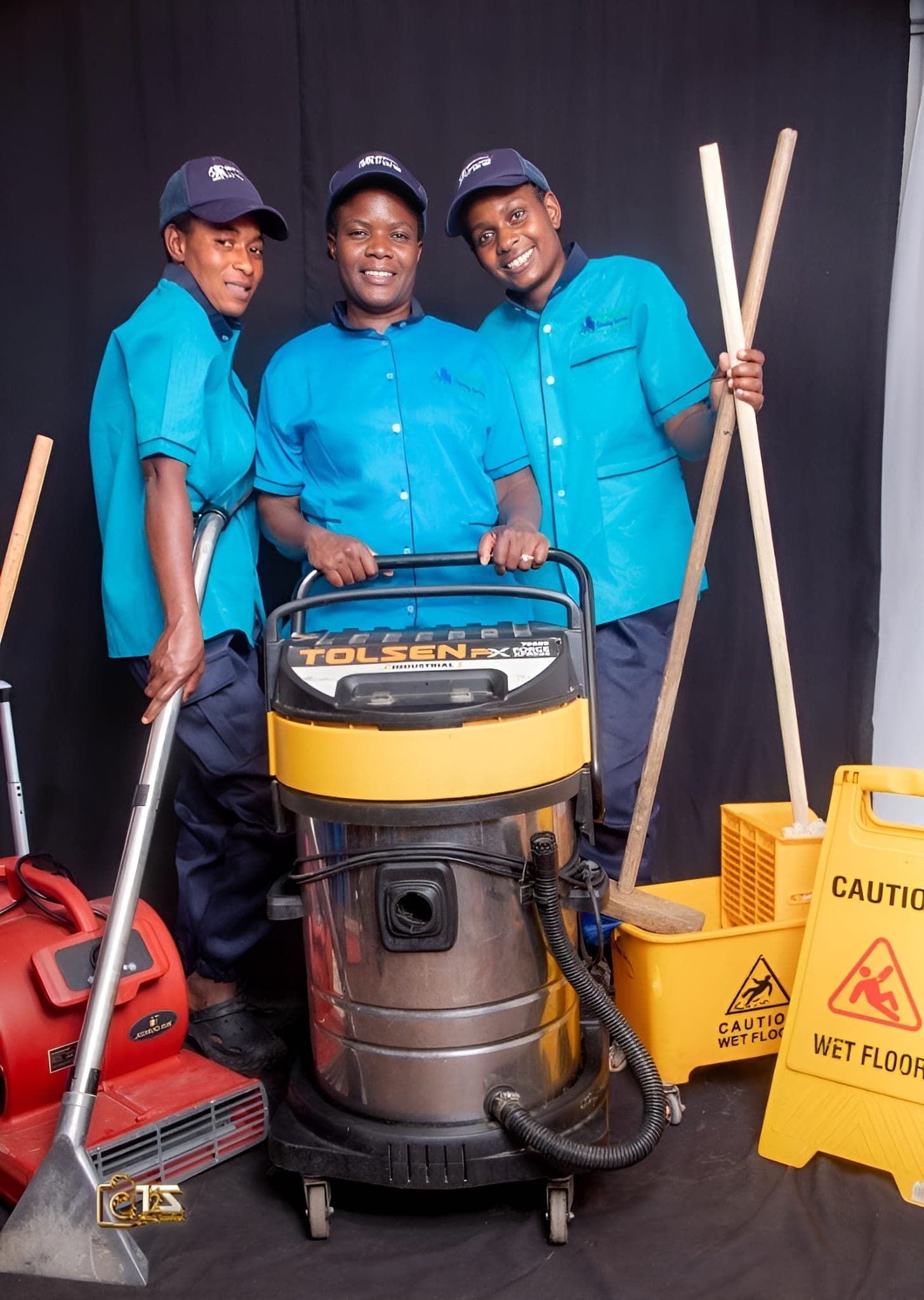 Three Brinancy cleaners in teal uniform with mops and caution signage